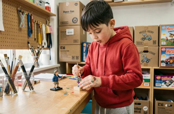 Garçon concentré peignant une figurine créative dans un atelier d'art enfantin bien équipé